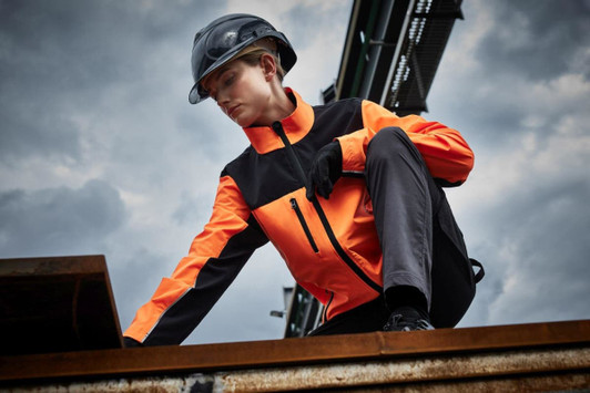 A work jacket in orange and black, featuring a zip and pockets, worn by a person on a construction site.