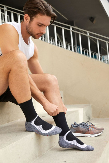 Black sport socks with a grey and white design, worn by a man sitting on steps beside running shoes.