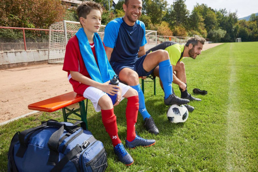 Team Socks in red and blue worn by players seated on a bench, with a soccer ball and gear on the grass field.