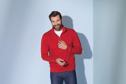 A red Round-Neck Zip jumper with a zippered collar, worn by a smiling man against a blue background.