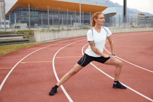 A white Ladies Running-T on a model stretching on a running track, paired with black shorts and sneakers.