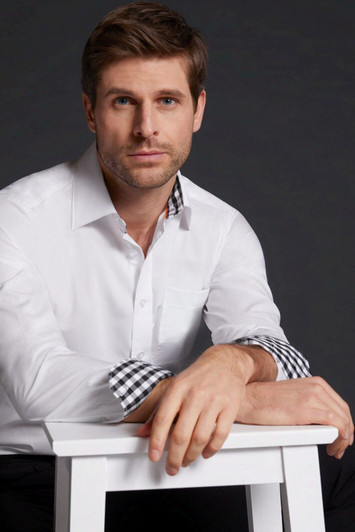 A plain white button-up shirt with checkered cuffs, worn by a man seated on a white stool. The background is dark.