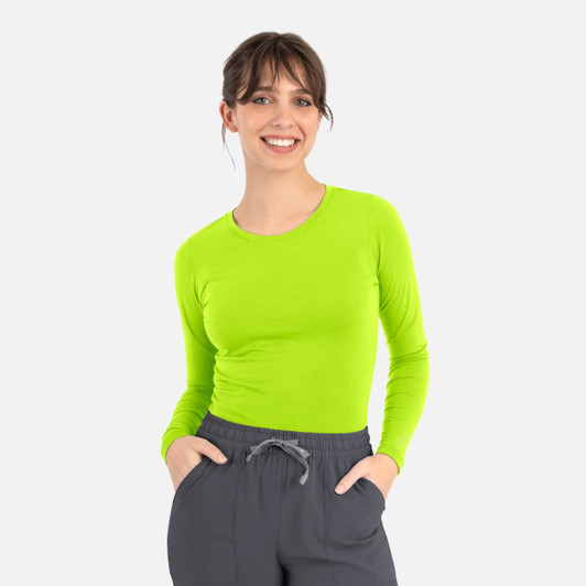 A woman is wearing a bright lime green long-sleeve tee paired with grey pants. The tee features a logo.