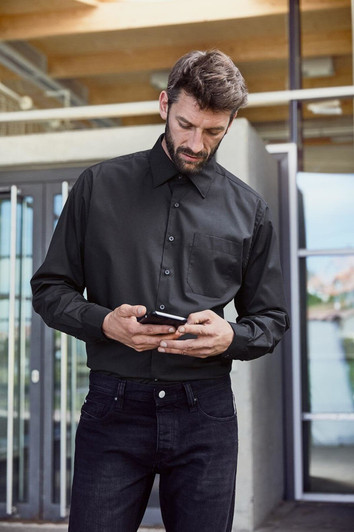 A black long-sleeved business shirt with a button-up front and a chest pocket, worn with dark jeans.