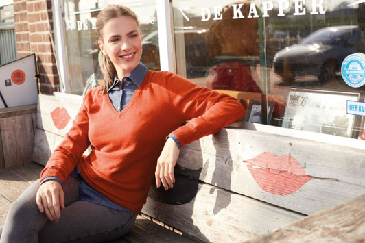 A woman wearing an orange ladies V-neck pullover sits on a wooden bench outside a café.