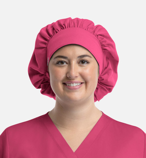 A unisex bouffant scrub cap in vibrant pink, featuring a gathered design, worn by a smiling person.