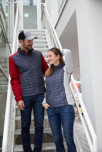 A grey and red knitted hybrid jacket is worn by a man and a woman, standing on a staircase. Both wear casual jeans.