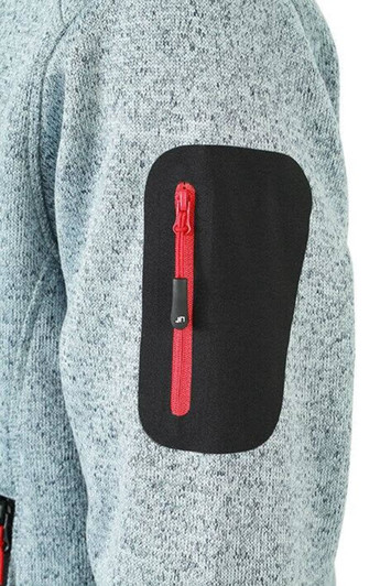 A grey knitted fleece jacket with a black patch on the sleeve, featuring a small red zip pocket.