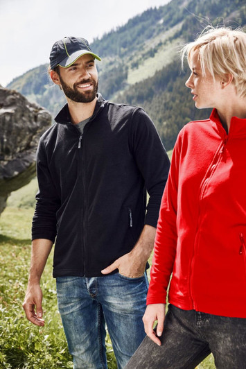 A couple stands outdoors wearing jackets; one in black and the other in red, with a logo on the jackets.