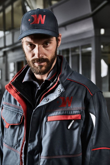 A workwear jacket in navy with red accents worn by a man. The jacket features pockets and has a logo.