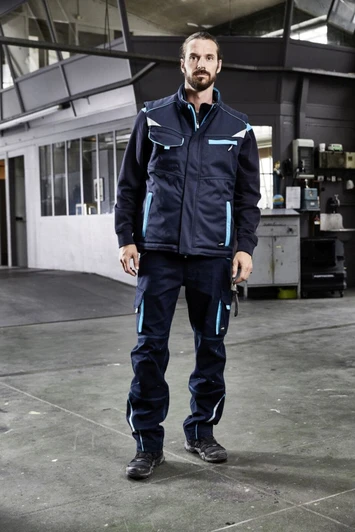A padded work vest in navy blue with light blue accents, featuring pockets and a logo, worn by a person indoors.