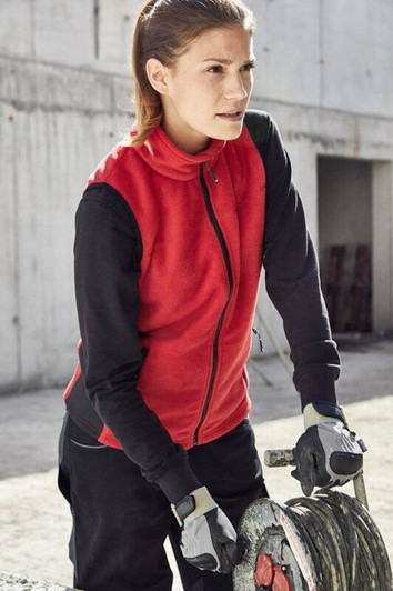 A red fleece vest worn by a woman, paired with black long sleeves and gloves, set in a work environment.