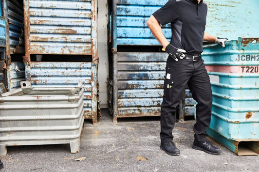 Black workwear cargo pants are worn by a person next to blue and grey storage containers. The pants feature pockets.