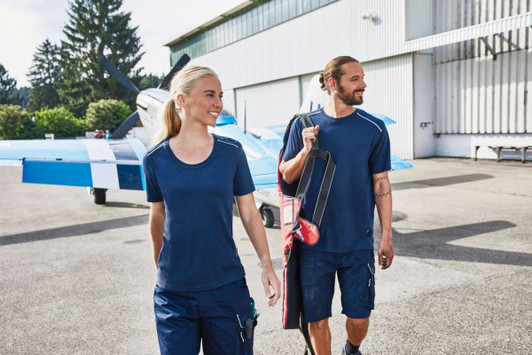 A navy blue men's workwear T-shirt, featured with a logo, alongside a model in a similar colour and setting.