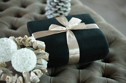 A black fleece blanket tied with a cream ribbon, placed on a tufted surface alongside decorative items.