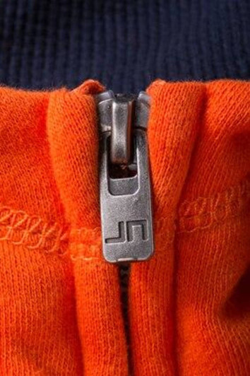 A zip on a hoodie featuring navy blue and vibrant orange fabric, with a metallic zipper and branding.
