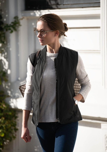 A stylish black puffer vest worn over a light top, paired with jeans, and set against a bright background.