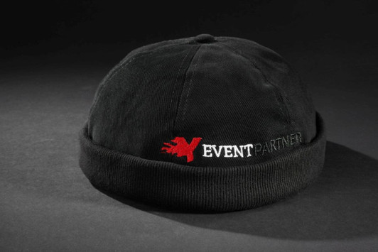 A black 6 panel chef cap with a folded brim and a logo featuring red text on the front.