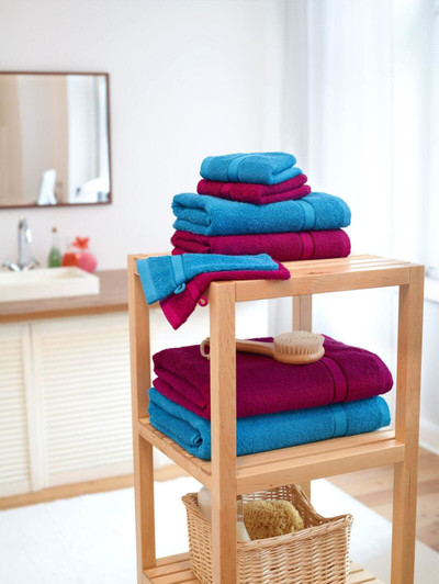 A stack of bright blue and deep red guest towels arranged on a wooden shelf, with a brush and a basket nearby.