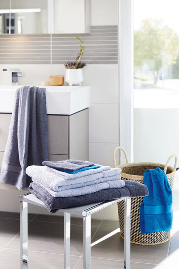 A collection of flannel hand towels in grey and blue, neatly arranged on a metal stool beside a woven basket.