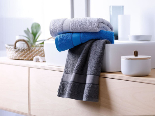 Three hand towels in shades of grey, blue, and light grey are neatly folded on a wooden surface with decorative items.