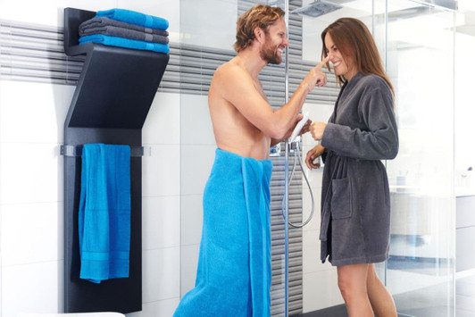 A couple in a bathroom, one wrapped in a vibrant turquoise bath sheet, the other in a grey robe, interacting playfully.