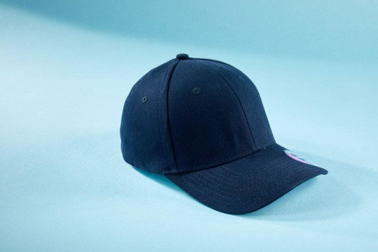 A navy blue 6 panel elastic fit baseball cap with a logo on the side, resting on a light blue background.