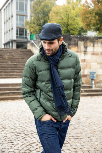 A man wearing a green puffer jacket, a grey cap, and a dark scarf, walking down stone steps in an outdoor setting.
