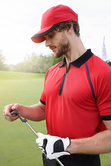 A red 5 panel sports cap worn by a man in a red polo shirt, holding a golf club on a green. The cap features a logo.