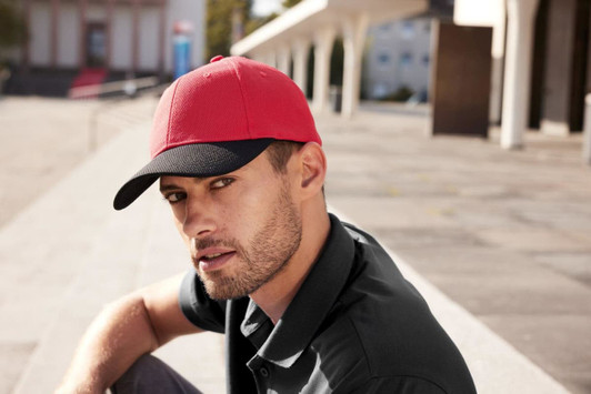 A red and black 6-panel mesh cap featured on a man, set against an outdoor background. The cap has a logo.