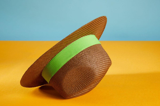 A brown Traveller Hat with a green band, featuring a wide brim, displayed against a blue and orange background.