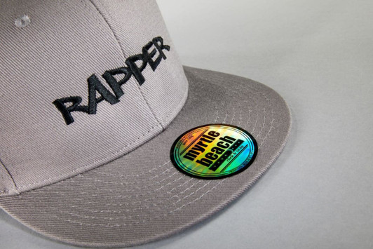 A grey cap featuring "RAPPER" embroidered on the front and a branded sticker on the peak.