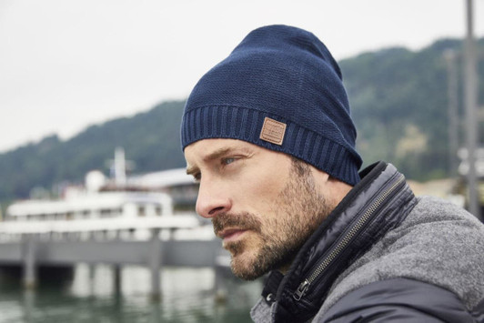 A cotton hat in navy blue worn by a man, featuring a small logo on the side, with a scenic waterfront background.