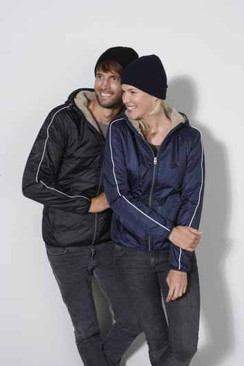 A man and woman wear matching jackets in black and navy, each sporting a knitted beanie, in a casual pose.