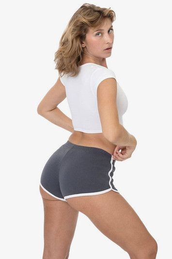 A model wearing grey interlock running shorts with white trim, paired with a white crop top, facing away from the camera.