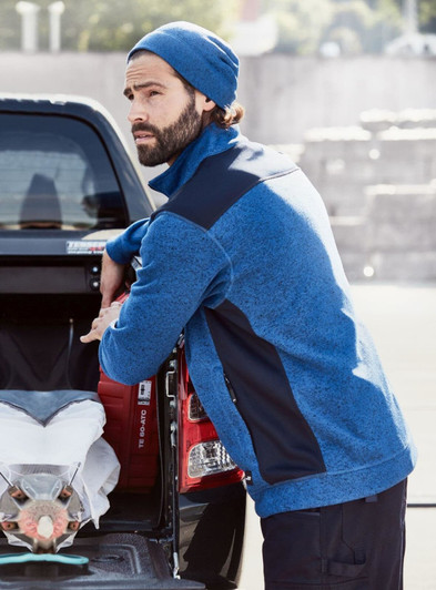 A knitted fleece workwear beanie in blue worn by a man leaning against a truck, showcasing a casual outdoor setting.