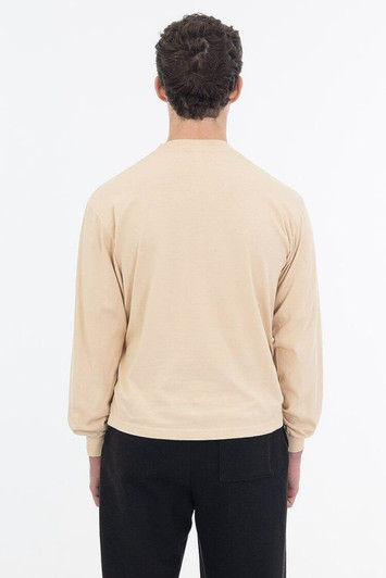 A long sleeve garment dye crewneck tee in a soft beige colour, displayed from the back. Features a subtle logo.