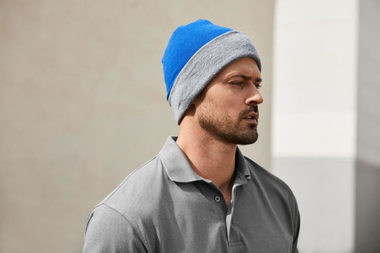 A reversible beanie featuring blue and grey colours, worn by a man in a grey polo shirt.
