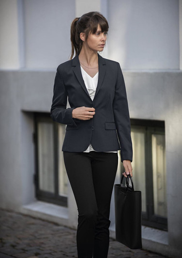 A woman in a fitted navy blazer and black pants holds a black bag, standing in an urban setting.