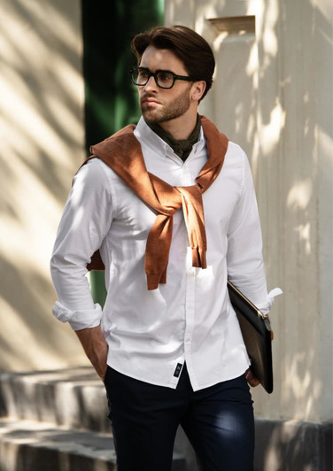 A slim fit white button-up shirt is worn by a man with brown accents, styled with a brown sweater draped around his shoulders.