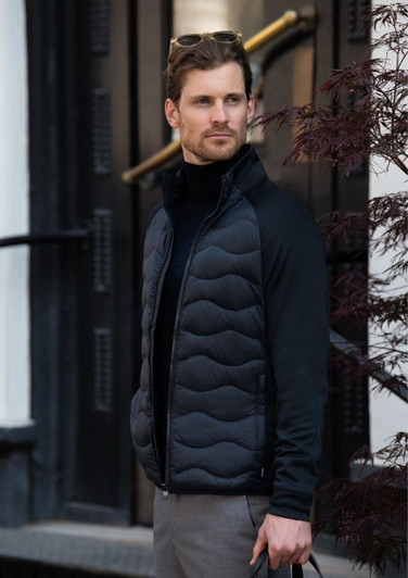 A man wearing a black puffer jacket with a zip front, standing outside near a building entrance.