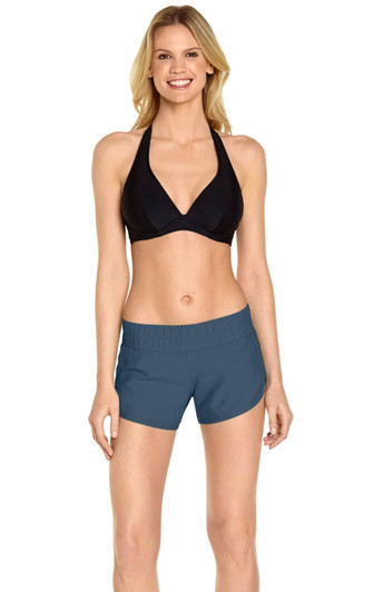 A model wearing women's swim shorts in a blue hue, paired with a black bikini top. The shorts feature a logo.