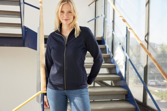 A navy ladies jacket with a zip front, worn by a model standing on a staircase. The jacket has a logo.