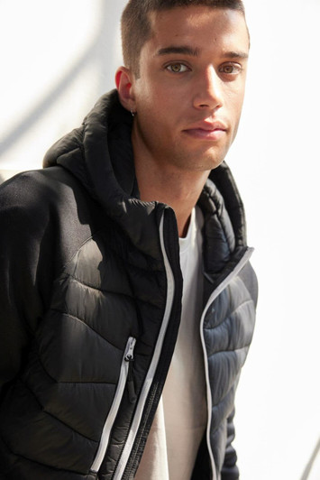A men's hybrid jacket in black, featuring a zip closure and a hood, modelled by a young man.