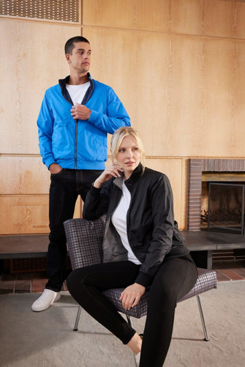 A blue blouson jacket worn by a man, alongside a black jacket worn by a woman sitting on a chair. Both have logos.
