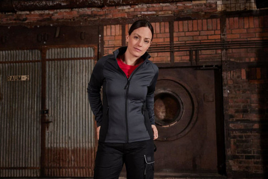A stretch fleece jacket in dark grey, featuring a zippered front and a collar, displayed in an industrial setting.