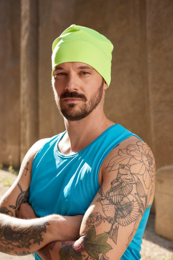 A bright yellow running beanie worn by a man with tattoos, dressed in a blue tank top, posing outdoors.