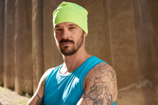 A running beanie in bright fluorescent yellow worn by a man with tattoos, dressed in a blue tank top.