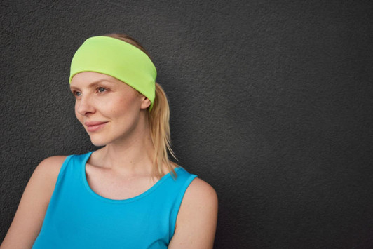 A running headband in bright lime green worn by a woman with blonde hair, against a dark background.