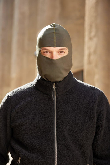 A green balaclava worn by a person in a black fleece jacket. The background is blurred, highlighting the product.